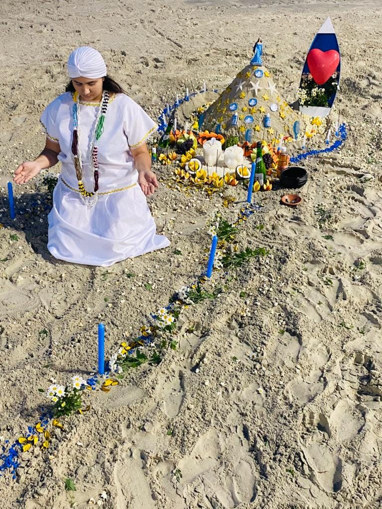Vidente Dyana ajoelhada na areia da praia realizando oferenda a Iemanjá